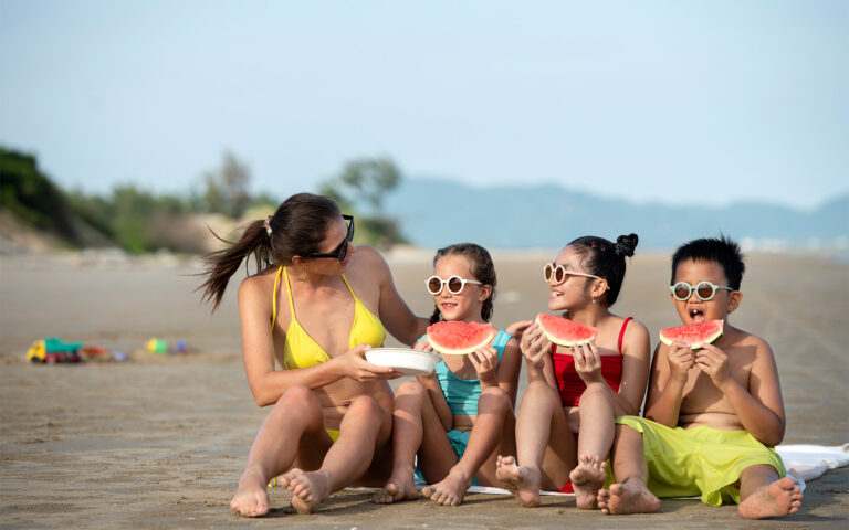 Family eating watermelon slices on a sunny sand beach