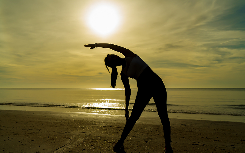 Woman stretching on beach during sand conditioning exercise routine.