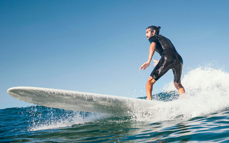 Man surfing on a wave wearing a black wetsuit.