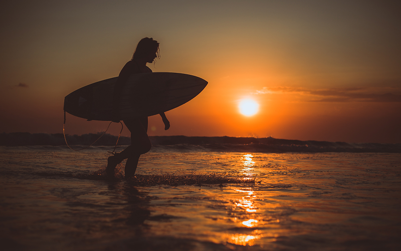 Silhouette of a surfer carrying a surfboard at sunset.